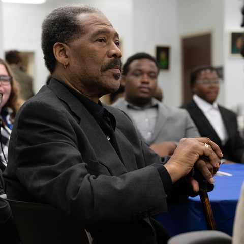 A distinguished gentleman with a cane listens attentively during a Black Alumni Networking event at Indiana State University, with other attendees in the background.